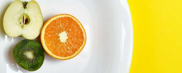 Top view of the sliced orange apple and kiwi fruit at the white dish lies on the bright yellow background. Healthy food, detox, diet concept