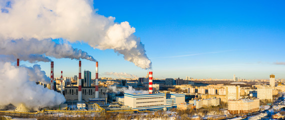 power plant pipes and cooling towers on the background of the panorama of the winter city against blue sky