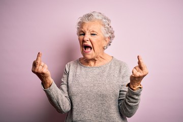 Senior beautiful woman wearing casual t-shirt standing over isolated pink background Showing middle finger doing fuck you bad expression, provocation and rude attitude. Screaming excited - obrazy, fototapety, plakaty