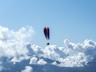 A man flying on a paraglider over the mountains on a background of blue sky with clouds