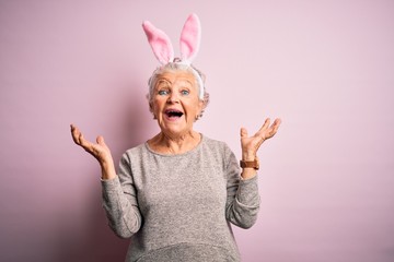 Senior beautiful woman wearing bunny ears standing over isolated pink background celebrating mad...
