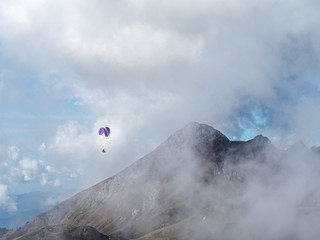 A man flies through a cloudy haze above the mountains on a paraglider