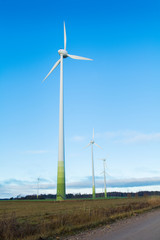 Wind electricity generator, visible green farming fields, grass, trees and blue skies with clouds