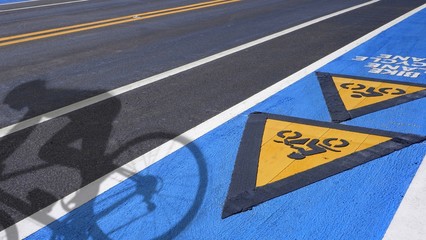 Shadow of cyclist with bicycle road sign and bike lane text on asphalt road. Separate bicycle lane for riding ecological green urban transport concept