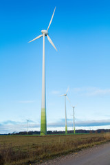 Wind electricity generator, visible green farming fields, grass, trees and blue skies with clouds