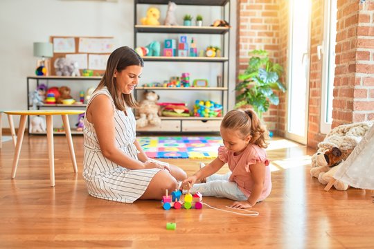Beautiful teacher and blond student toddler girl playing with wooden train at kindergarten