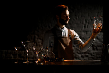 Professional male bartender standing on the bar counter rubs the glass cup with a rag