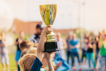 Happy kids in school sports team rising golden cup. Boys winning sports championship. Child holding...