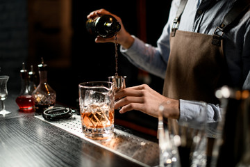 Bartender pouring a alcoholic drink from the bottle to a steel jigger