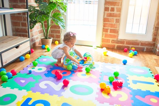 Beautiful caucasian infant playing with toys at colorful playroom. Happy and playful wth colorful balls at kindergarten.