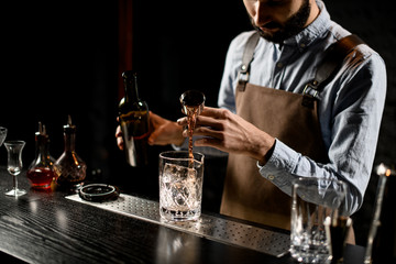 Bartender pouring a golden alcoholic drink from the steel jigger to a glass