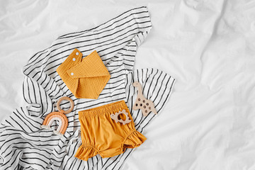 Orange shorts and bib with baby toys. Set of  kids clothes and accessories for summer  on  bed....