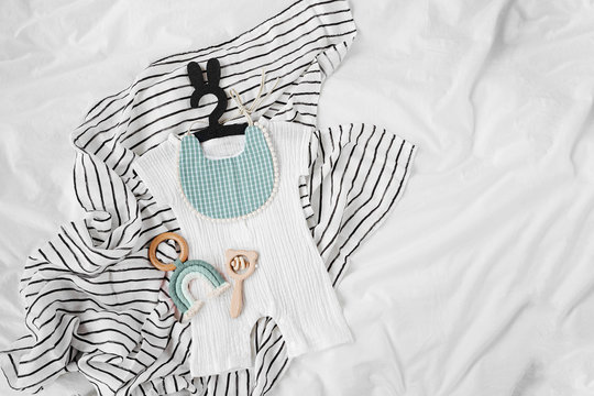 White romper and blue bib with baby toys. Set of  kids clothes and accessories for summer  on  bed. Fashion childs outfit. Flat lay, top view