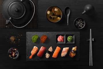 Sushi rolls, sashimi set, miso soup and teapot, on dark wooden table, Japanese food, top view. - obrazy, fototapety, plakaty