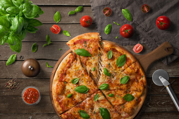 Pizza on wooden board, with tomatoes and basil, Italian style on old wooden table, top view.