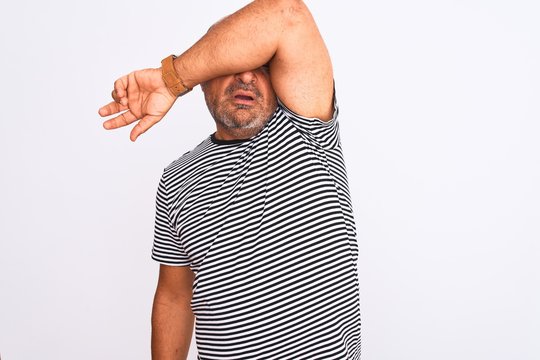 Middle age handsome man wearing striped navy t-shirt over isolated white background covering eyes with arm, looking serious and sad. Sightless, hiding and rejection concept