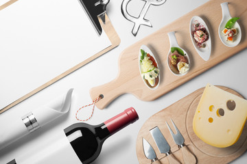 Blank restaurant menu template, on white table with wine bottle canapes and cheese, top view.