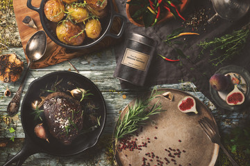 Delicious outdoor table with steak, baked potatoes on dark background, top view. Rustic food...
