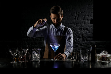 Professional bartender spraying with a bitter on the blue alcoholic cocktail in a martini glass