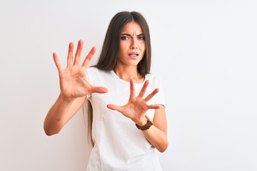 Young beautiful woman wearing casual t-shirt standing over isolated white background afraid and terrified with fear expression stop gesture with hands, shouting in shock. Panic concept.