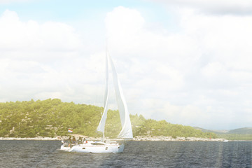 Sailing yacht in a fair wind passes by a rocky green shore of Dalmatian riviera in the sanny summer day.  Mediterranean region of  Europe. Adriatic sea in Croatia country. Luxury lifestyle on the rest