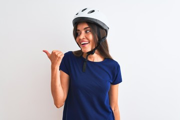 Young beautiful cyclist woman wearing security bike helmet over isolated white background smiling with happy face looking and pointing to the side with thumb up.