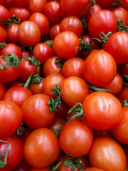 small red round tomatoes with small green ponytails on a supermarket counter awaiting buyers