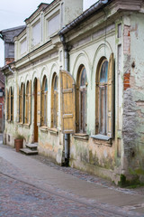Old, rusted building with arched windows and with orang, brown old wooden window shutters