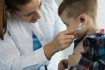 Portrait of beautiful woman practitioner standing in modern clinic office with little boy. Kids patients playing with stethoscope and trying listening to his breath. Medicine and healthcare concept