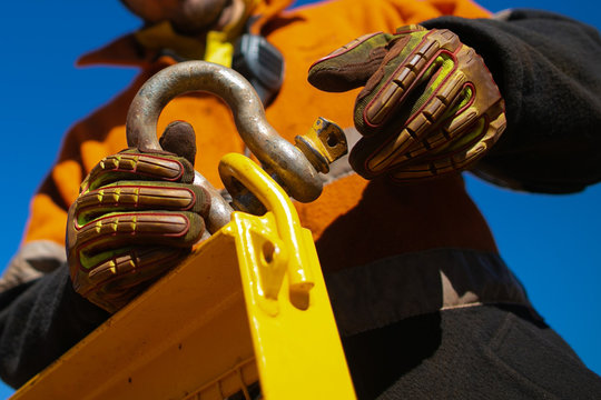Close up rigger high risk worker wearing safety heavy duty glove, safety helmet fastening pin into D- shape shackle industry crane lifting lug gate prior lift at construction site Perth city