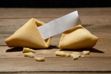 Close up of fortune cookie with blank paper inside and cookie crumbles on a bamboo board