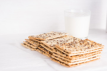 Stack of crispy wheat cakes with sesame , flax and sunflower seeds with glass of milk on a white wooden background. vegetarian food, eco food concepts
