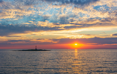 Ocean sunrise with small lighthouse on a island.