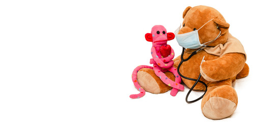 Pediatrician concept. Teddy bear in medical mask with stethoscope presented as pediatrician and cute monkey with red heart as patient isolated on white background. Banner. Copy space.