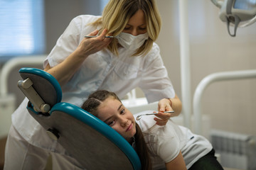 Dentist woman doing teeth checkup of little girl looking with fear sitting in stomatology clinic.