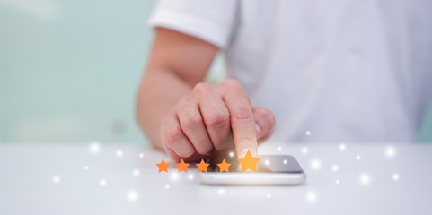 close up on customer man hand pressing on smartphone screen with gold five star rating feedback icon and press level excellent rank for give score point to review the service business concept	