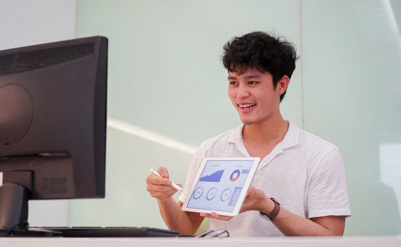 close up young asian employee man video conference with marketing team and showing market research by tablet and explaining report in ouse for quarantine and work from home concept