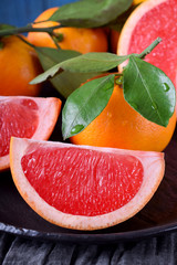Slices of red grapefruit and whole mandarins with green leaves on the black plate