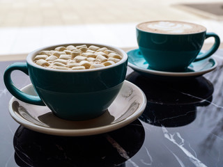 Two green mugs with cocoa and cappuccino, close-up. Delicious hot drinks on the background of a bright window. Coffee break for two in a coffee shop