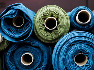 Blue and green rolls of knitted fabric. Woven factory or warehouse - obrazy, fototapety, plakaty
