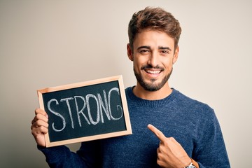 Young man holding blackboard with strong message standing over isolated white background very happy pointing with hand and finger