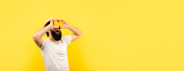 bearded hipster man holding lemon slices in front of eyes, over yellow background, panoramic...