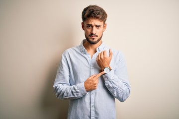 Young handsome man with beard wearing striped shirt standing over white background In hurry...