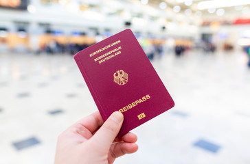 A hand holds a german passport in an airport terminal - obrazy, fototapety, plakaty