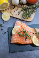 Fresh salmon on slate plate and ingredients on dark background.