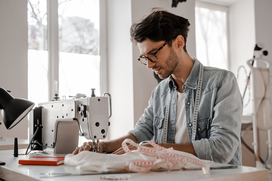Stylish and fashionable clothes designer man sews at a sewing machine. Sewing, design work, tailoring studio, tailor, designer clothes, manufactory, in the process of creative development