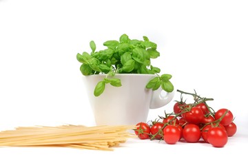 closeup of bowl with cherry tomatoes, spaghetti and basil jar on a white background