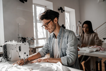 Focused on the sewing process tailors sit sewing at their sewing machines. Sewing, design work, tailoring studio, tailor, designer clothes, manufactory, in the process of creative development