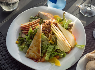 Close up view of white plate with fresh vegetable salad with homemade goat cheese, lettuce, pear and caramelised nuts on sea food restaurant table at la Palma. Selective focus.