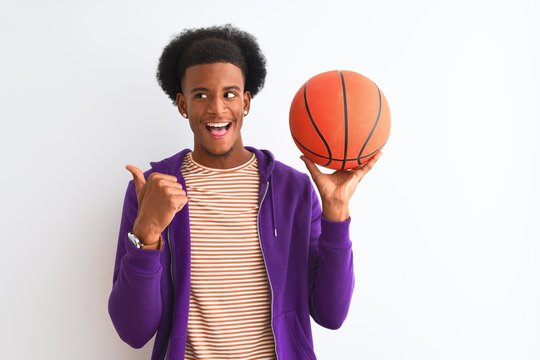 Young african american sportsman holding basketball ball over isolated white background pointing and showing with thumb up to the side with happy face smiling